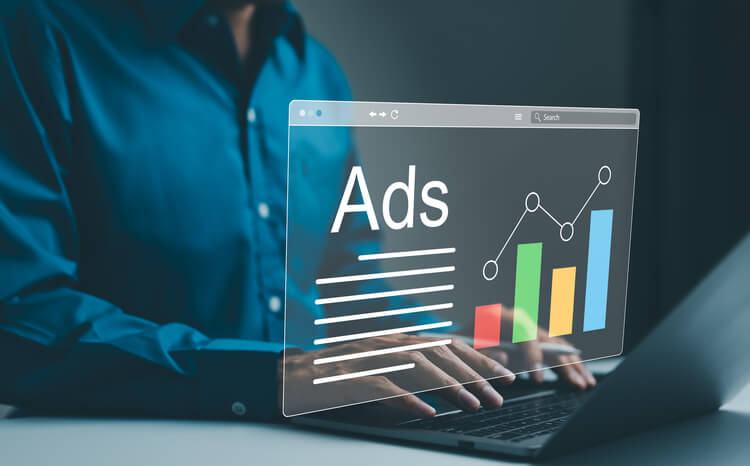 A man types on a laptop, with a floating digital interface displaying “Ads” beside upward-trending graphs. The visual highlights pay-per-click advertising strategies, performance tracking, and data-driven marketing growth analytics.