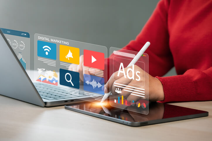 A person using a tablet stylus interacts with a futuristic digital interface showing “Ads,” charts, and icons for SEO, email, video, and social media marketing, representing modern digital advertising strategies and PPC campaigns.