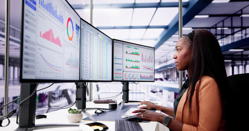 A digital marketing coordinator reviewing campaign analytics on multiple monitors in a Vancouver office